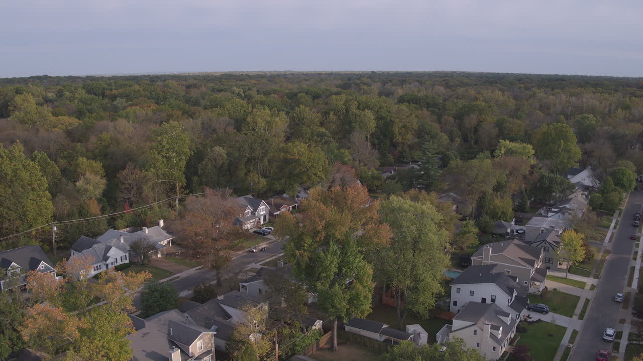 Tilt down over suburban neighborhood in Autumn as a car drives down the street and pulls into a driveway
