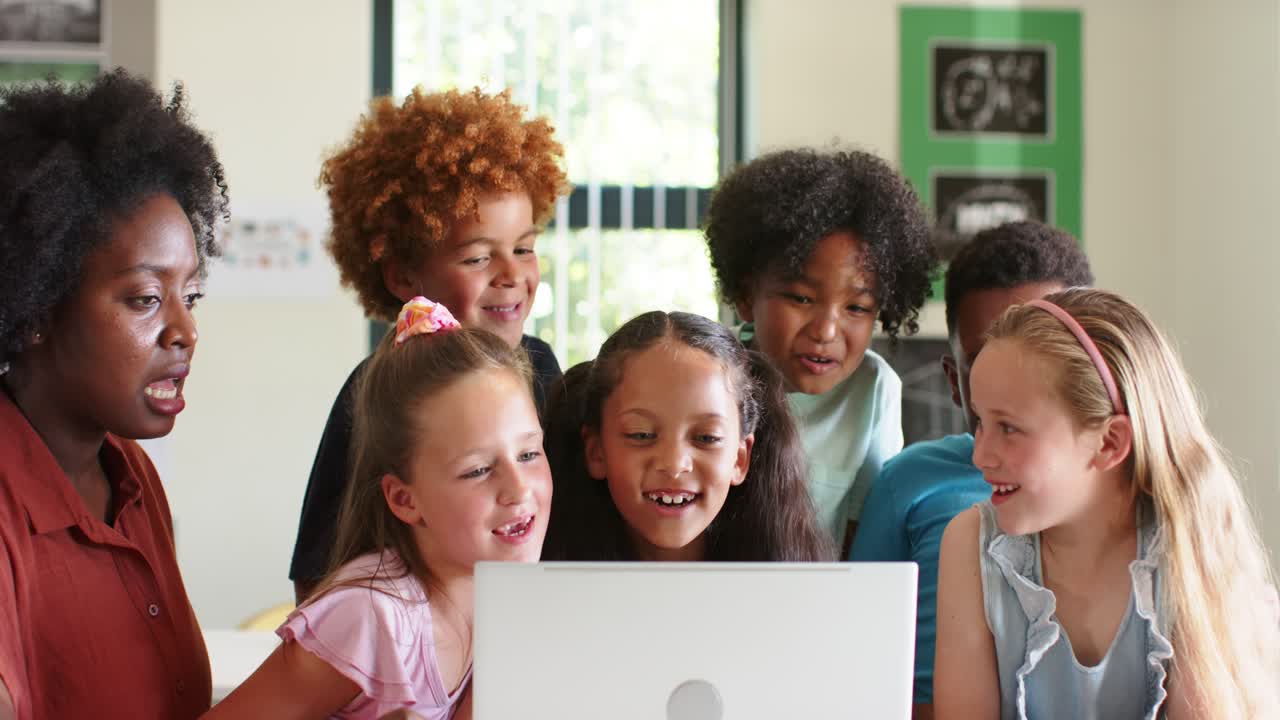 Un'insegnante afroamericana con studenti di diverse etnie indica un laptop in classe, guidando i bambini che si sporgono.