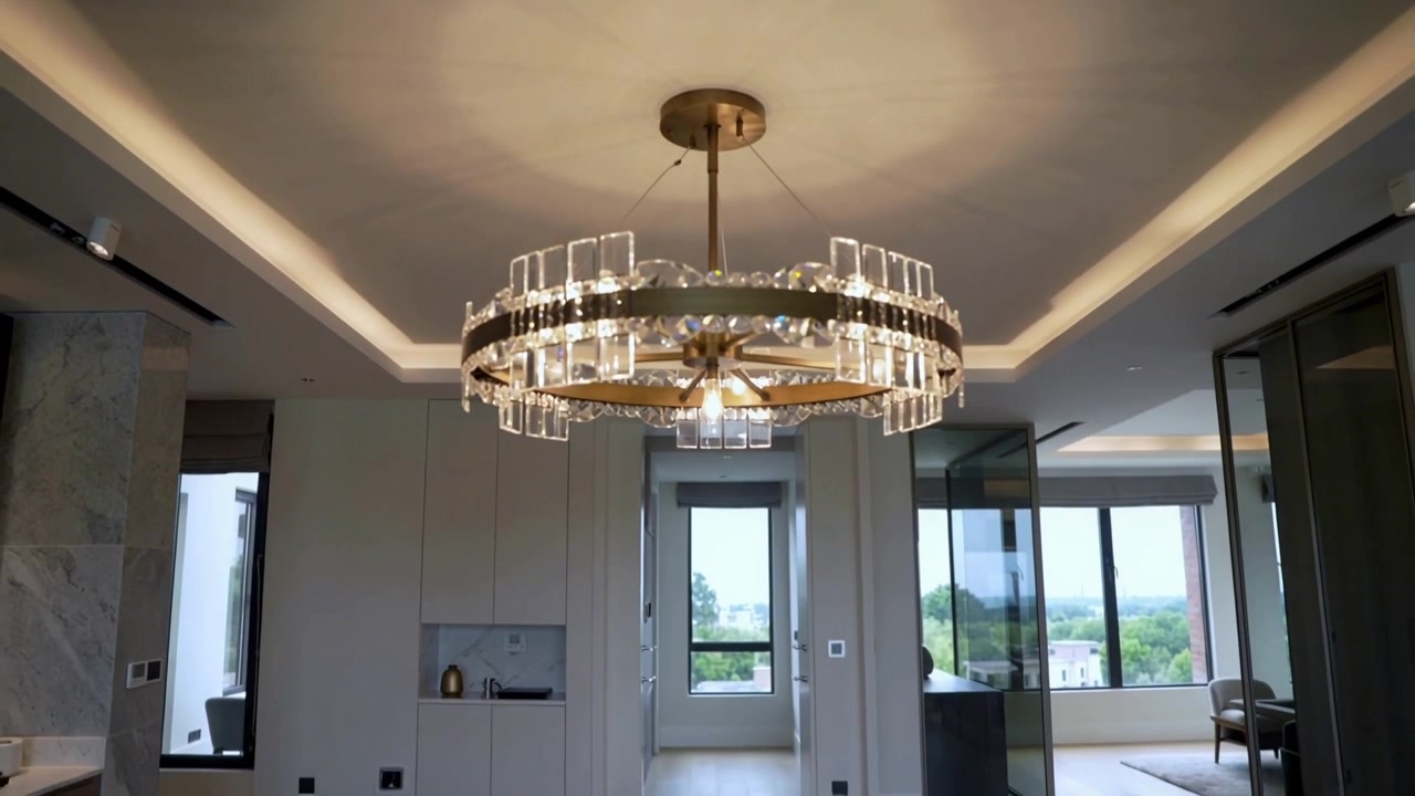 Pulling back camera revealing chandelier in modern living area, showing cove lighting and windows