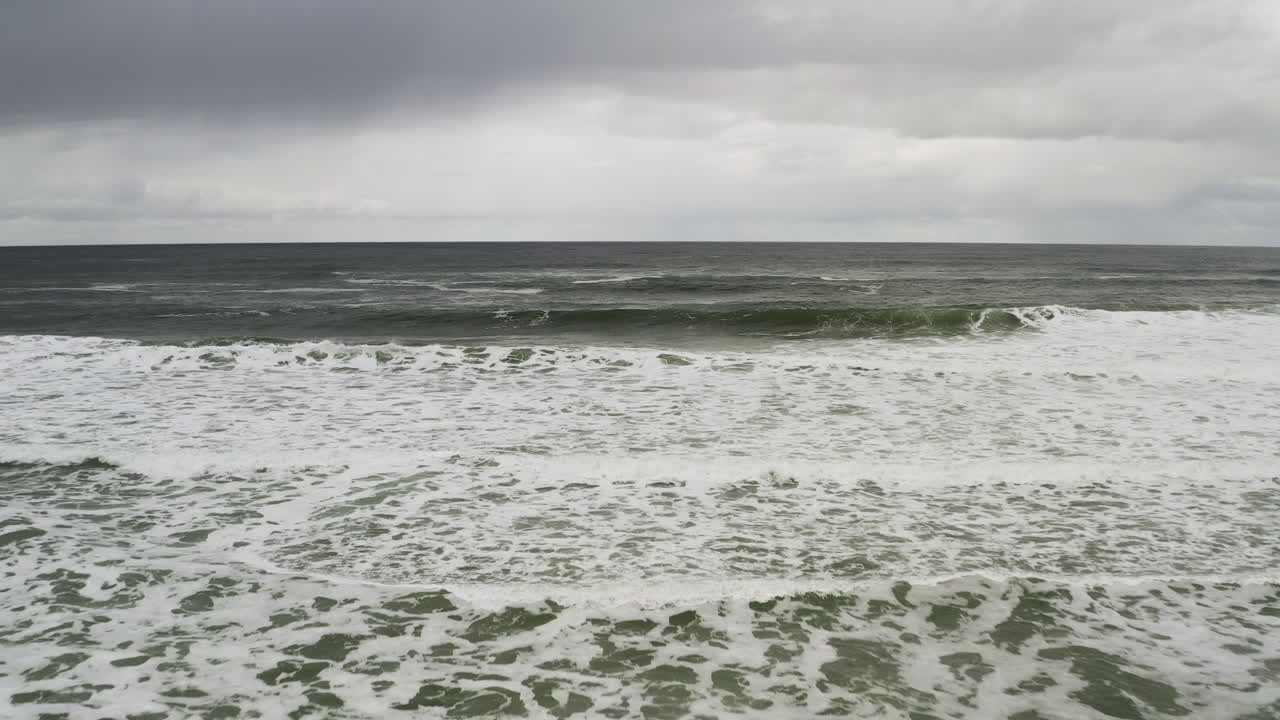 네스코윈 오리건 해안의 구름이 가득한 하늘과 함께 모래 해변을 따라 바다의 거품 모양의 물결의 공중 전망, 거꾸로 공중