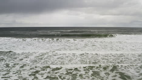 Aerial-Oceanfront-View-Of-Ocean-Foamy-Waves-Along-Sandy-Shore-With-Overcast-Sky,-Neskowin-Oregon-Coast,-backwards-aerial