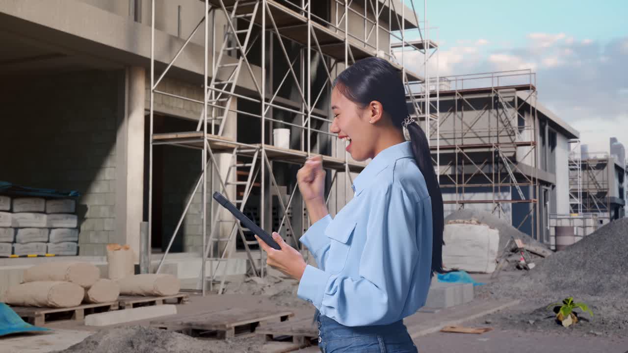 Side View Of Asian Female With Her Tablet At Construction Site in Progress to New House, She Raises Her Fist Up With Screaming Goal After Check On The Tablet