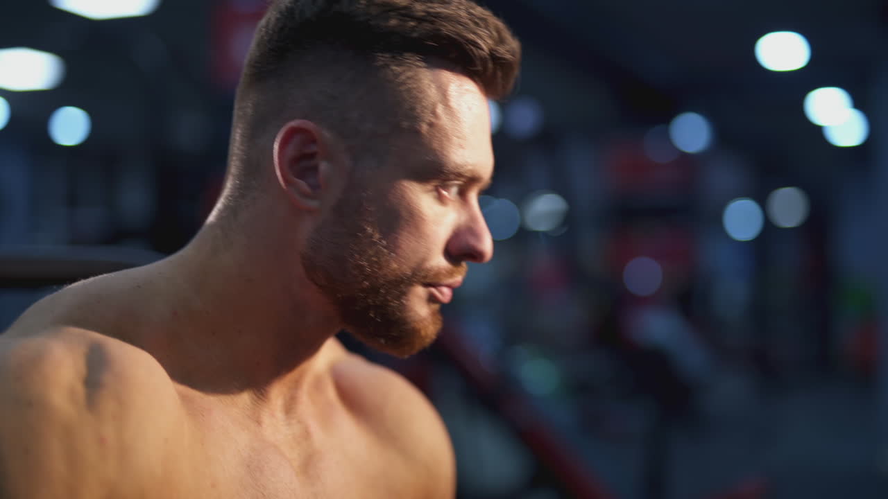 Tired bodybuilder resting after training. Young handsome athlete sitting and drinking water. Close-up portrait of a sportsman.