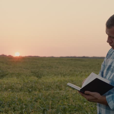 farmer makes notes in a notebook and stands in a field