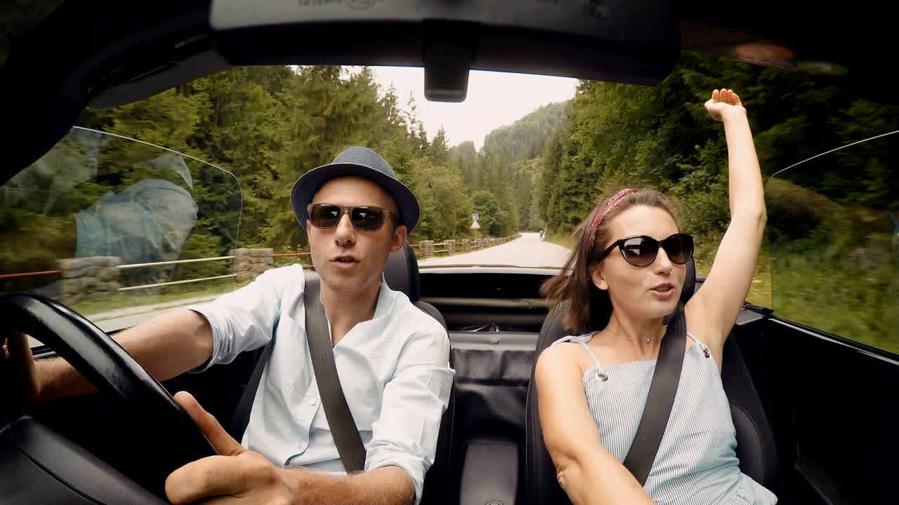 imágenes en 4k de una pareja en el descapotable cantando.