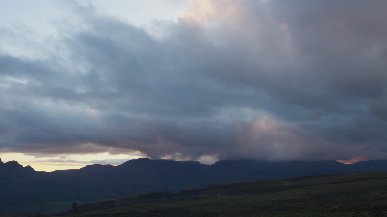 Fast moving clouds drifting over dramatic mountain silhouettes during vibrant sunset, capturing stunning landscape of Gran canaria with dynamic sky and atmospheric light