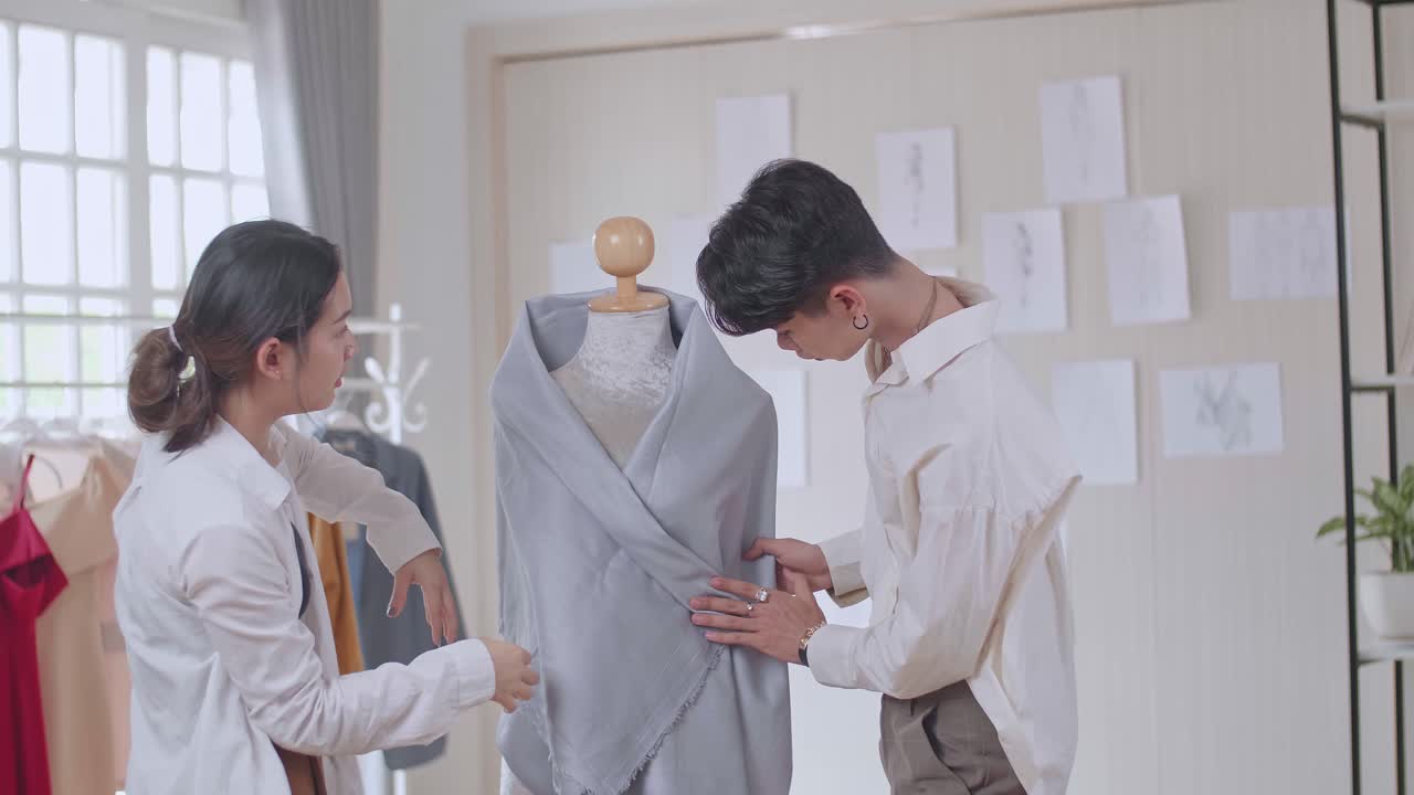 Two Young Asian Fashion Designers Adjusting Fabrics On A Tailored Mannequin