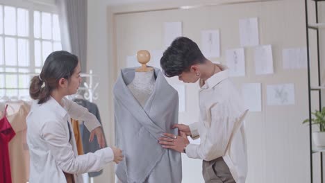 two young asian fashion designers adjusting fabrics on a tailored mannequin