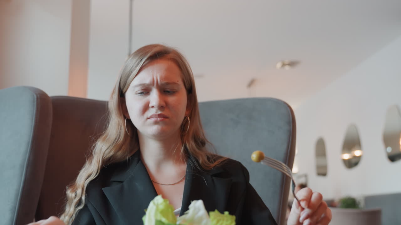 Kaukasisk kvinde med afskyelig reaktion på oliven i smart bistro, udtryksfuld grimasse efter ubehagelig bid, kunde inspicerer salatkvalitet, diskret spænding i stilfuld blazer, indendørs lys