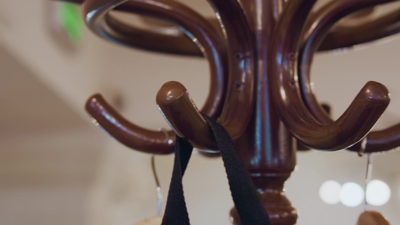 Close up of wooden coat rack with multiple hooks as hands hang and remove black fabric bags. scene features soft lighting indoor background elements like blurred architectural details