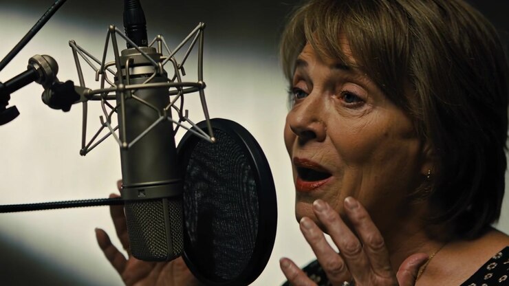 Cantante donna che inspira, canta e modella una ripresa vocale in studio, indossando una blusa scura, con microfono, spazio per il testo.