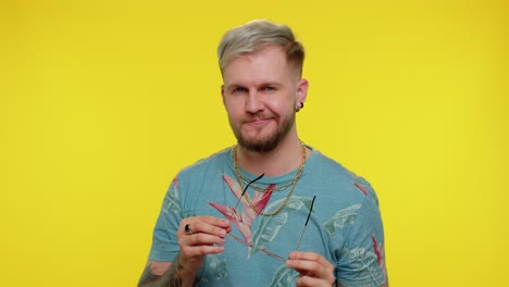 Sincere-cool-cheerful-stylish-man-in-blue-t-shirt-wearing-sunglasses,-charming-smile-on-yellow-wall