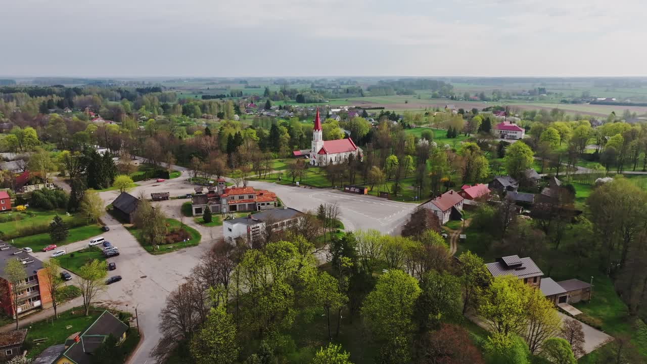 Dronekuva Rucavan kyläkirkon punaisesta katosta ja vihreistä pelloista, Latvia.