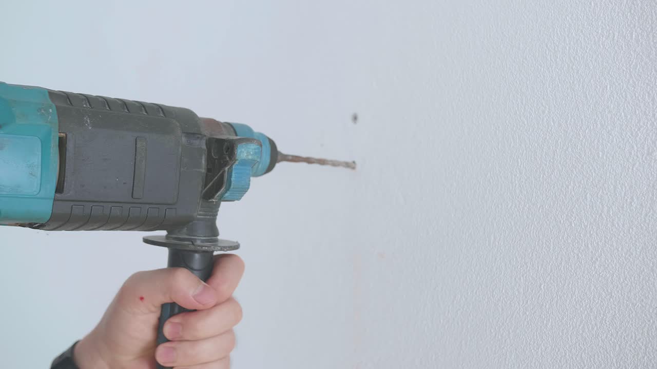 las manos del técnico del trabajador utilizan un taladro eléctrico para perforar la pared