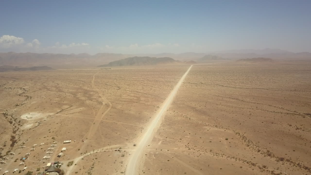 4K drone starts far behind a lone jeep on a dusty Namib Desert road, then flies forward, closing the gap and immersing the viewer in the vast, sun‑baked landscape.
