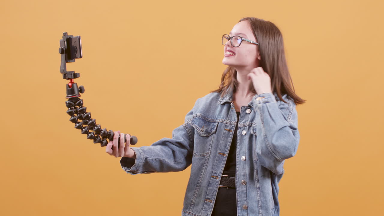 Young woman vlogging with smartphone on orange background