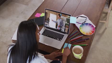 Caucasian-female-student-using-laptop-on-video-call-with-male-teacher,-making-notes