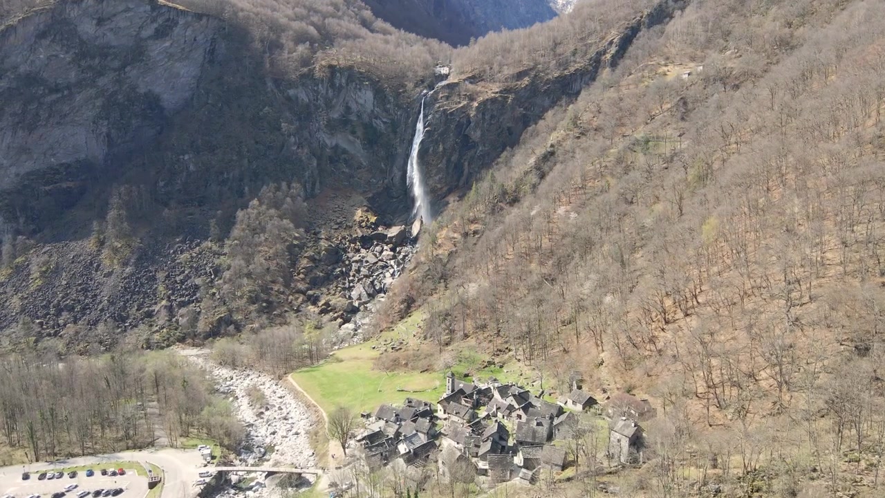 Ripresa aerea in dolly di Foroglio, Svizzera, un pittoresco villaggio alpino circondato da lussureggianti montagne verdi e una splendida cascata.