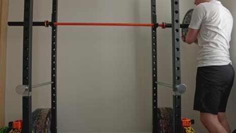 static shot of a man putting extra plates on a barbell in a squat rack