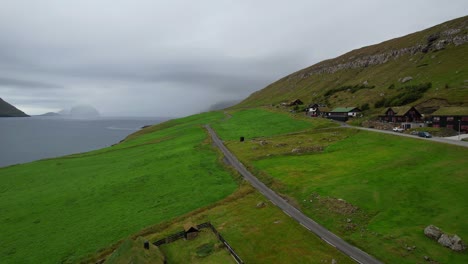 Backward-drone-over-Kirkjubour-village-on-Faroe-Islands-with-cabins-in-meadow-on-foggy-day