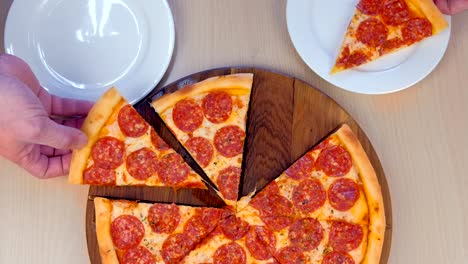 la gente toma una rebanada de pizza de salami en sus platos, vista de cerca desde arriba.