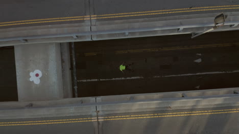 AERIAL:-Young-man-with-bright-green-shirt-laying-on-street-slow-Birds-eye-View-flight-over-Downtown-Los-Angeles-California-Main-Road-in-beautiful-Sunset-Light-rising-upwards