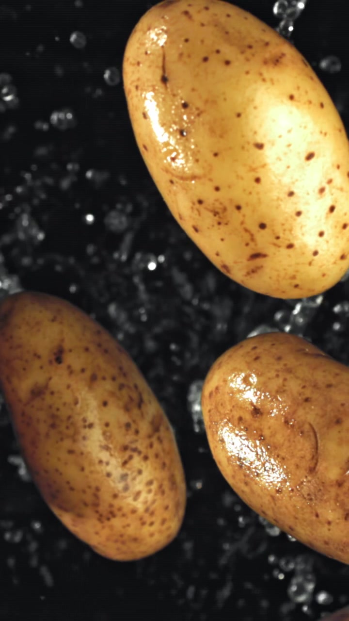 Patate fresche che vengono lavate con gocce d'acqua su sfondo nero