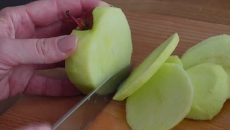 Side-view-of-a-woman-slicing-an-apple-into-chunks-to-use-in-a-healthy-portion-of-food-on-a-wooden-table-in-the-kitchen