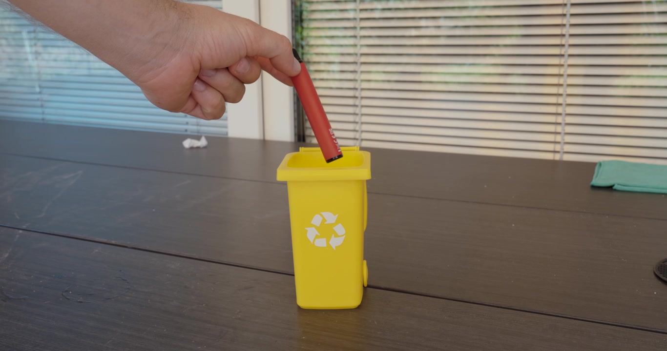 Person disposing of a used vape in a recycling container, representing responsible electronic waste disposal, battery recycling and environmental protection.