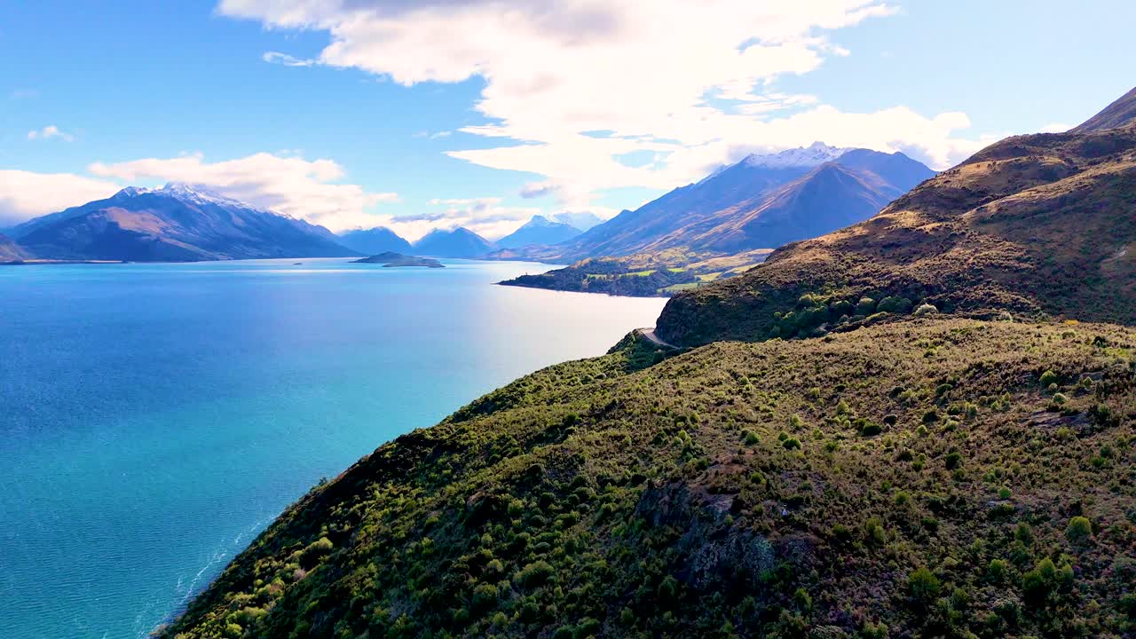 Un drone sorvola una strada panoramica di montagna e un lago turchese sotto la luce del giorno, ampia vista del paesaggio