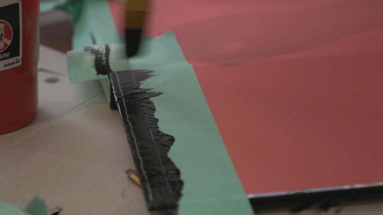 A Painter Applying Black Oil Paint Using A Paintbrush On The Red Paper - Close Up Shot