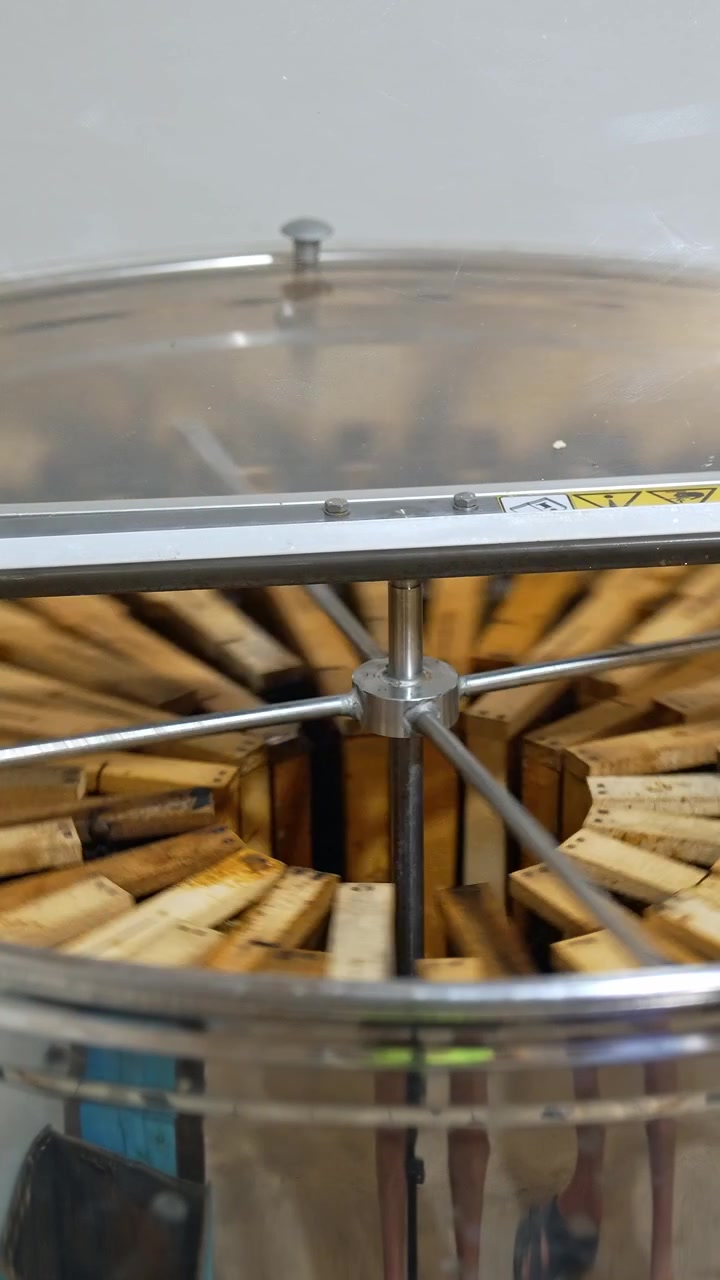 Working centrifuge machine for honey extraction from frames. Electric device spins honeycombs and slowly stops rotating. Vertical video