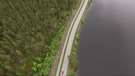 Beautiful-panoramic-drone-shot-of-a-quiet-road-in-Norway,-with-gorgeous-green-trees-and-a-calm-lake-on-a-cloudy-summers-day