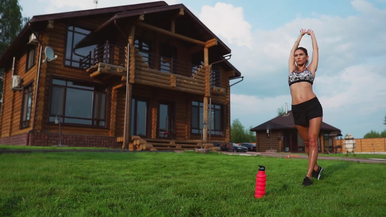 женщина на траве занимается йогой на фоне красивого дома. концепция здорового образа жизни