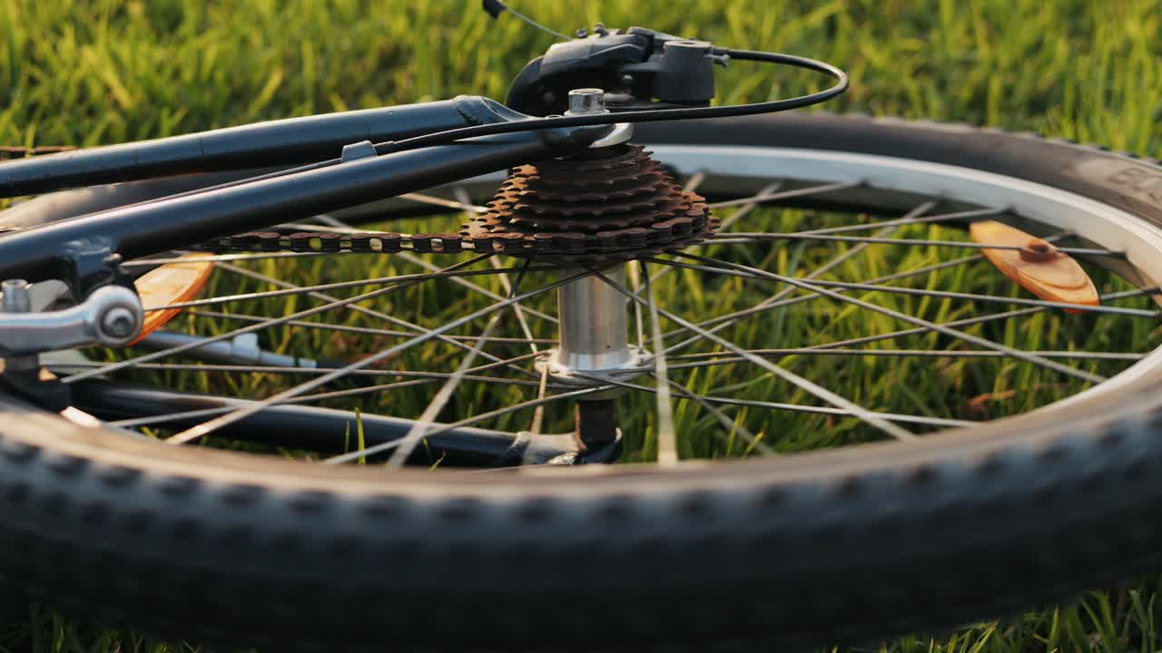 A stunning closeup photograph of a bicycle wheel resting in lush green grass during a magnificent sunset scene
