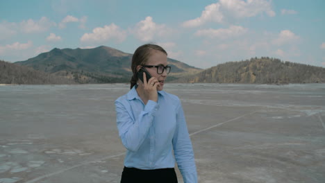 joven y hermosa mujer de negocios caminando por un campo vacío y hablando por teléfono celular