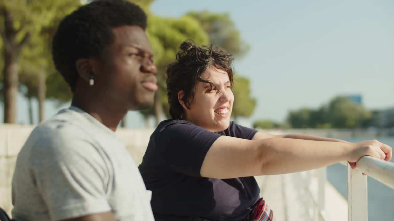 mujer joven sonriente mostrando algo a un amigo masculino en el muelle