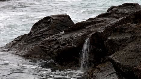 tiny waterfalls created over seaside rock as they get slammed by the crashing waves