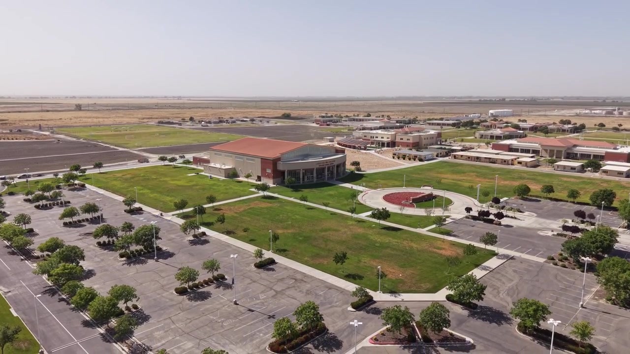 Descending drone view of the West Hills College campus in Lemoore, California, showcasing the modern architecture, empty parking lots, green spaces, and surrounding agricultural landscape