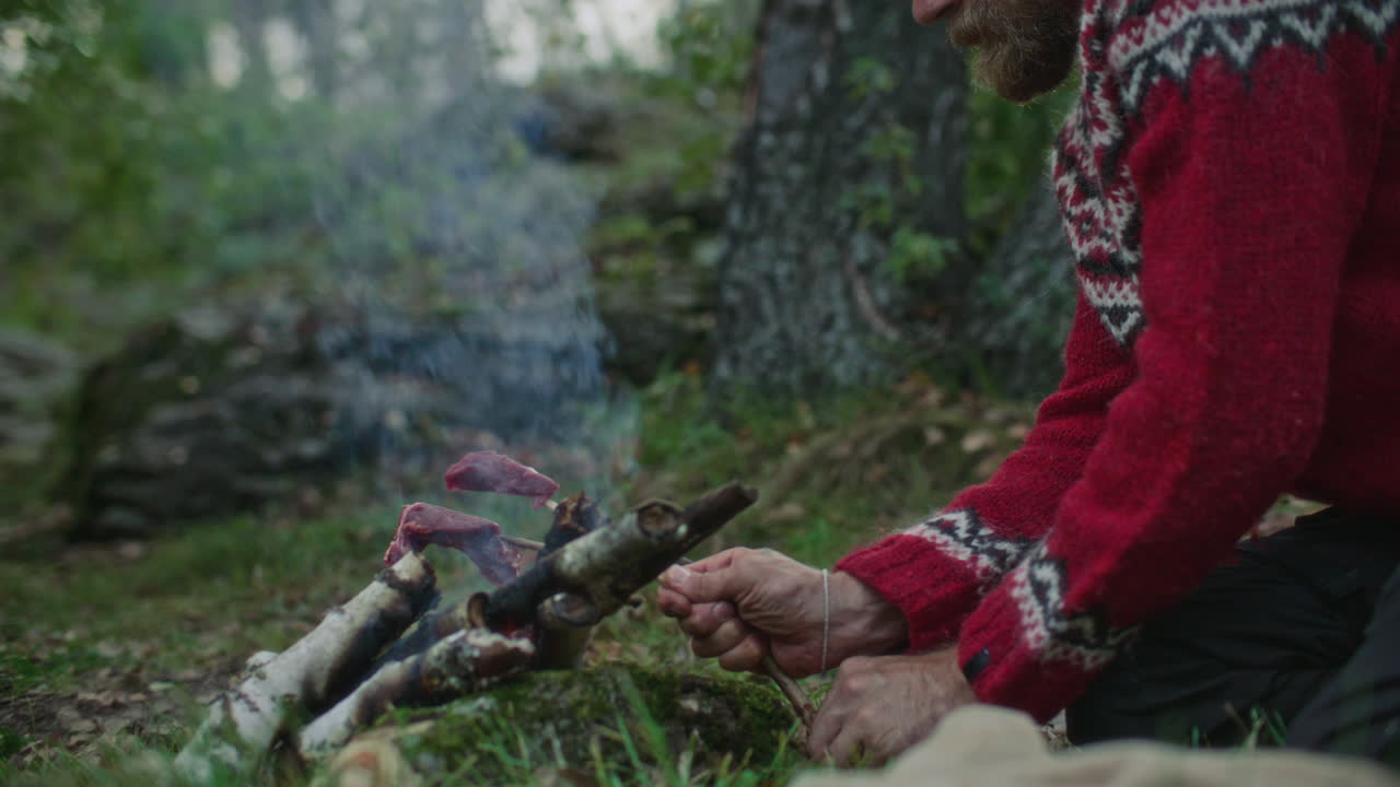 Close-Up of Man Roasting Meat Skewered on Stick over Campfire in Woods