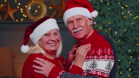 Smiling-married-senior-couple-grandparents-man-woman-in-living-room-celebrating-Christmas-together