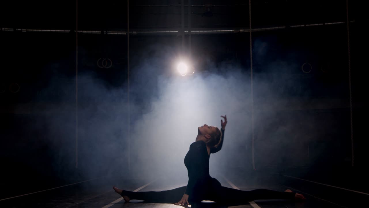 silhouette di ginnasta femminile che si allunga e balla nello studio buio