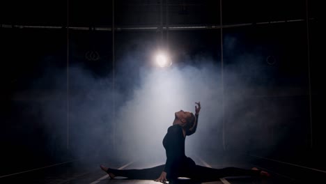 silueta de una gimnasta femenina estirándose y bailando en el estudio oscuro