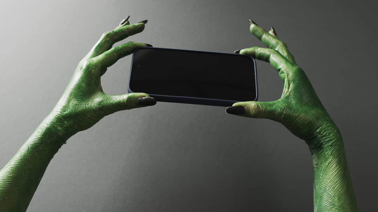 video de las manos del monstruo verde de halloween sosteniendo un teléfono inteligente con espacio de copia en un fondo gris