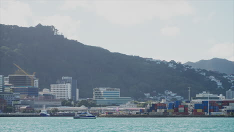 A-ferry-moves-across-the-bay-in-front-of-the-industrial-port-of-Wellington,-New-Zealand