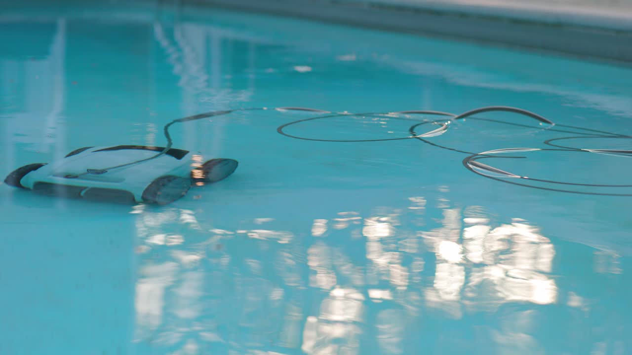 el robot eléctrico de limpieza de piscinas limpia la piscina con un cable de alimentación que flota en agua clara y reflectante