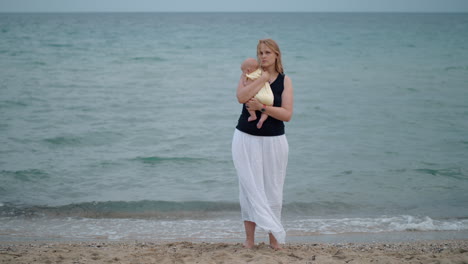 Mutter-Mit-Verlorenem-Blick-Hält-Ihr-Baby-Allein-Am-Strand-In-Der-Nähe-Des-Meeres