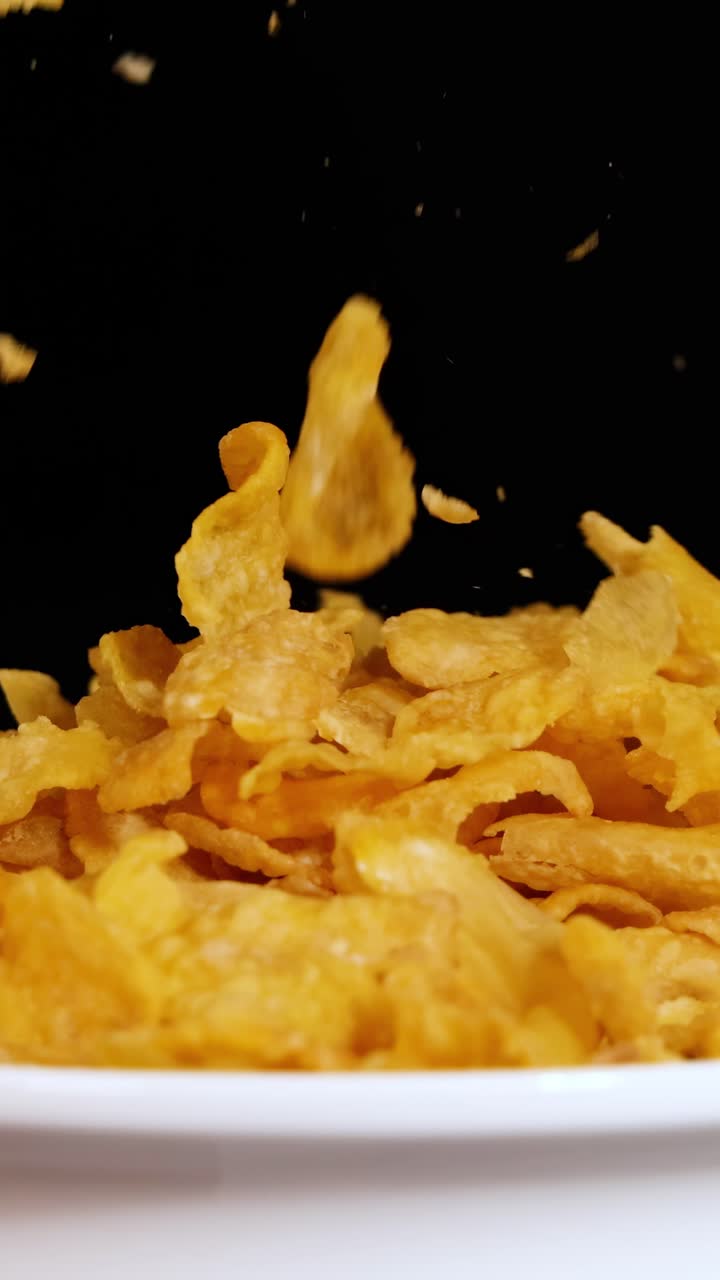 Fiocchi di mais cadono a cascata in una ciotola bianca su uno sfondo nero, creando una scena dinamica e visivamente suggestiva.