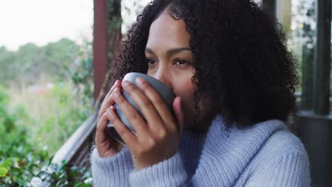 happy mixed race woman enjoying drinking coffee standing on balcony in countryside