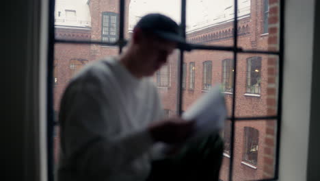 Man-reading-by-the-window-on-a-snowy-day,-urban-scene-outside